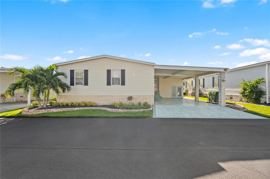 A single-story manufactured home with light siding, a brick base, and an attached carport — 39 EMDEN CIRCLE, PUNTA GORDA, FL