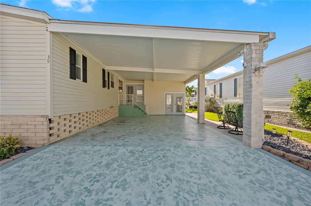 A covered carport with a textured concrete floor sits beside a light-colored manufactured home — 39 EMDEN CIRCLE, PUNTA GORDA, FL