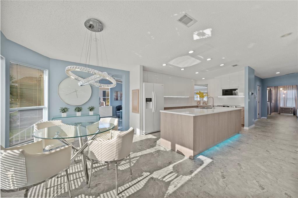 A modern kitchen and dining area features a glass table, white chairs, and a kitchen island — 39 EMDEN CIRCLE, PUNTA GORDA, FL