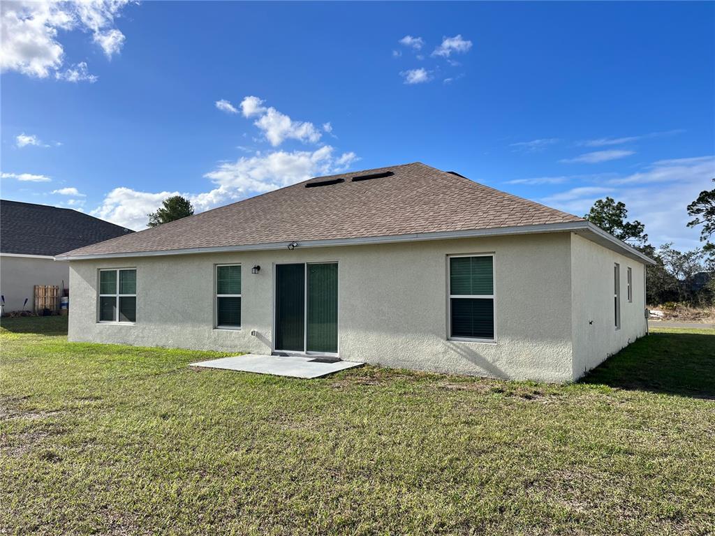 The rear exterior of a single-story stucco house features a sliding glass door and patio — 4441 PALMARITO STREET, SEBRING, FL