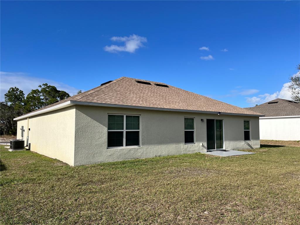 The rear exterior of a single-story house features tan stucco walls and a hip roof — 4441 PALMARITO STREET, SEBRING, FL