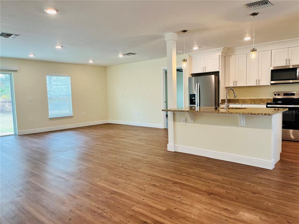 An open-concept kitchen with white cabinets and a breakfast bar overlooks a living area — 4441 PALMARITO STREET, SEBRING, FL