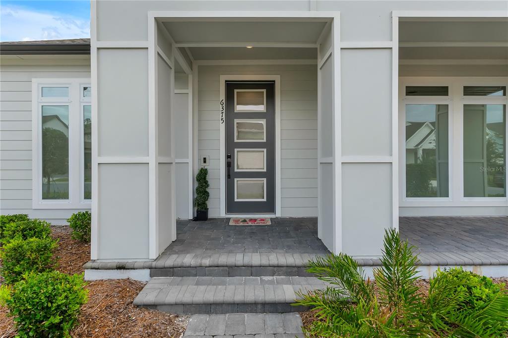 The exterior of a modern home features a gray front door with four glass panels — 6375 TRAILBLAZE BEND, ST CLOUD, FL