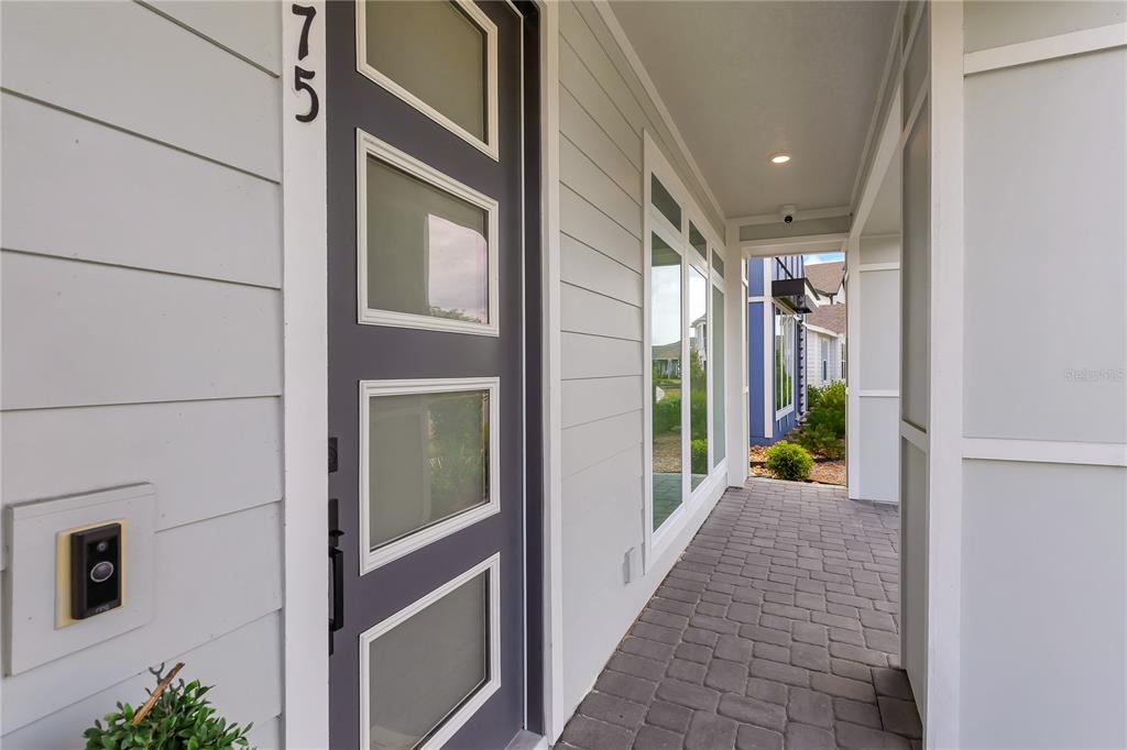 A gray front door with four glass panels sits beside a paved entryway walkway — 6375 TRAILBLAZE BEND, ST CLOUD, FL