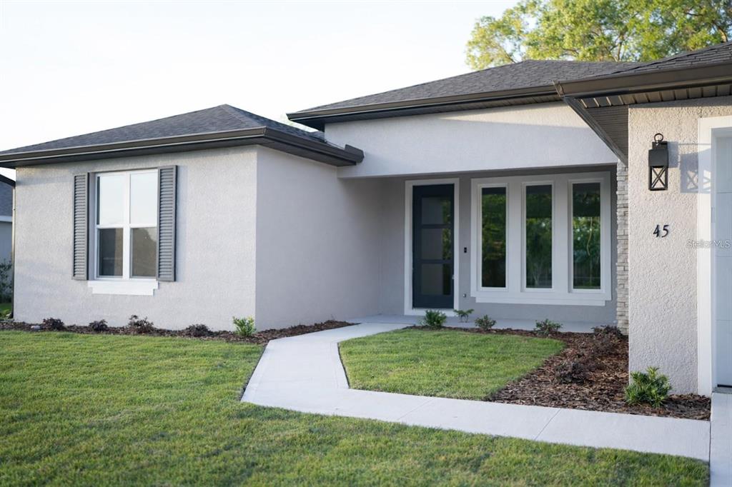 A single-story house with a light gray stucco exterior, dark trim, and a concrete walkway — 21 LAMAR LANE, PALM COAST, FL