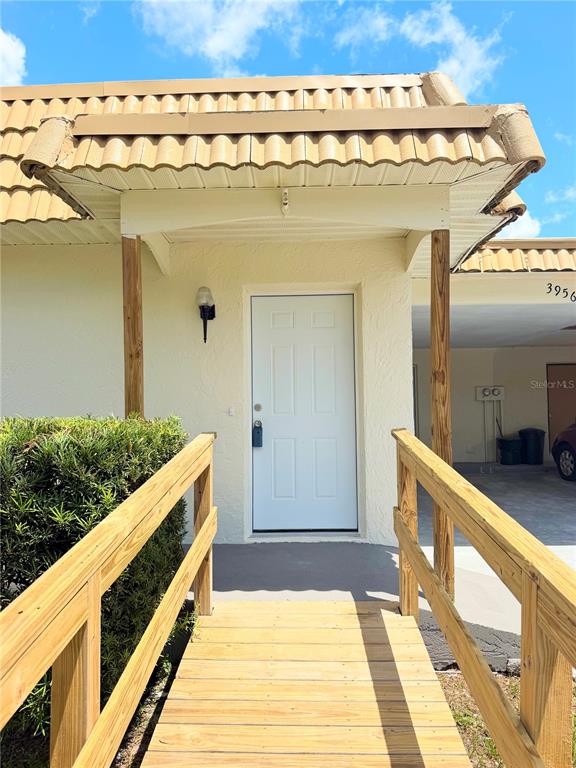 A wooden ramp leads to the white front door of a building with a tiled roof — 3956 EL CANTI CAMINO, NEW PORT RICHEY, FL