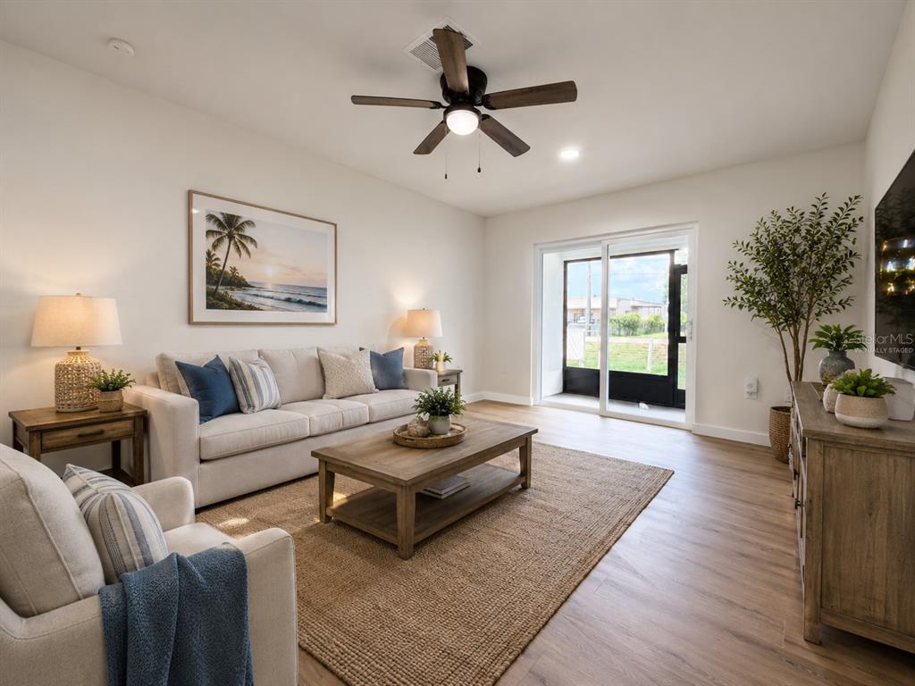 A living room features a beige sofa, wooden coffee table, ceiling fan, and sliding glass doors — 3956 EL CANTI CAMINO, NEW PORT RICHEY, FL