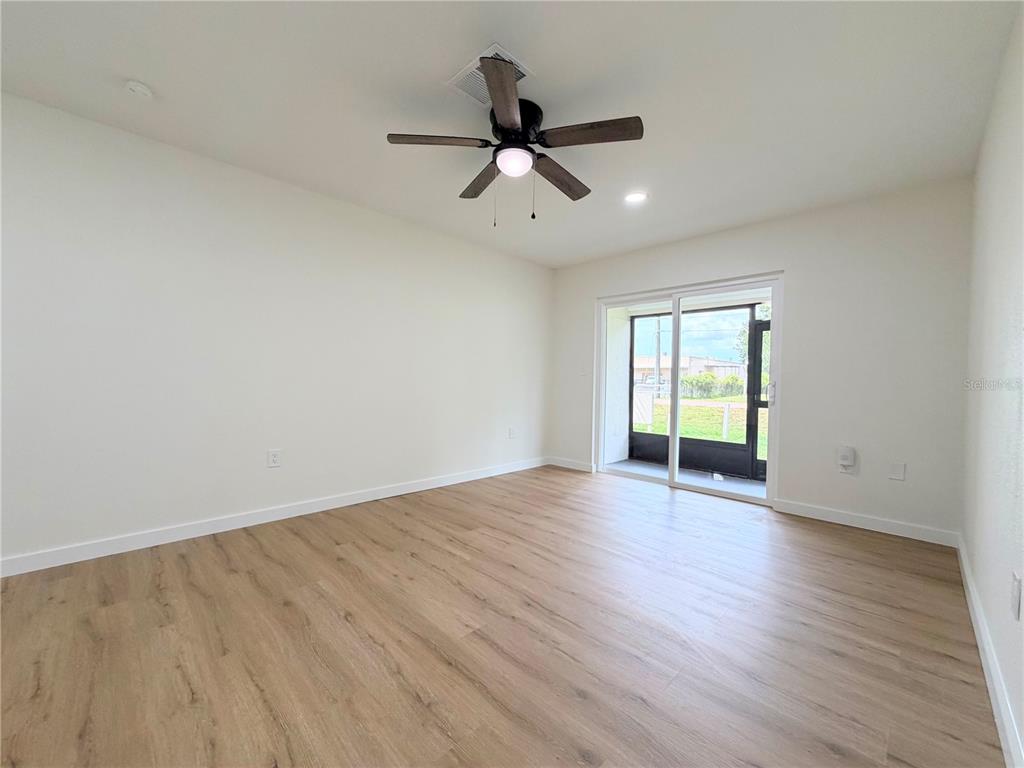 A bright room with light wood-look flooring, a ceiling fan, and a sliding glass door — 3956 EL CANTI CAMINO, NEW PORT RICHEY, FL