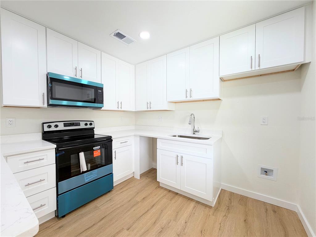 A kitchen with white cabinets, stainless steel appliances, and light wood-look flooring — 3956 EL CANTI CAMINO, NEW PORT RICHEY, FL