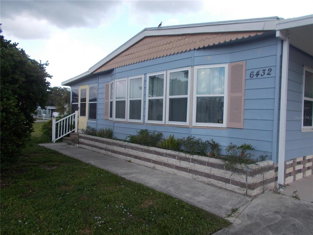 A light blue manufactured home features a brick planter box and a concrete walkway — 6432 KEENA COURT, NORTH PORT, FL