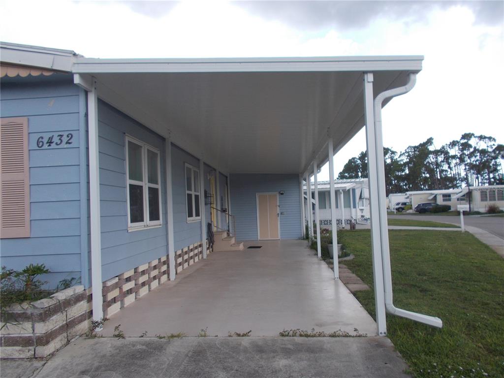 A light blue mobile home features a large covered carport and a concrete driveway — 6432 KEENA COURT, NORTH PORT, FL