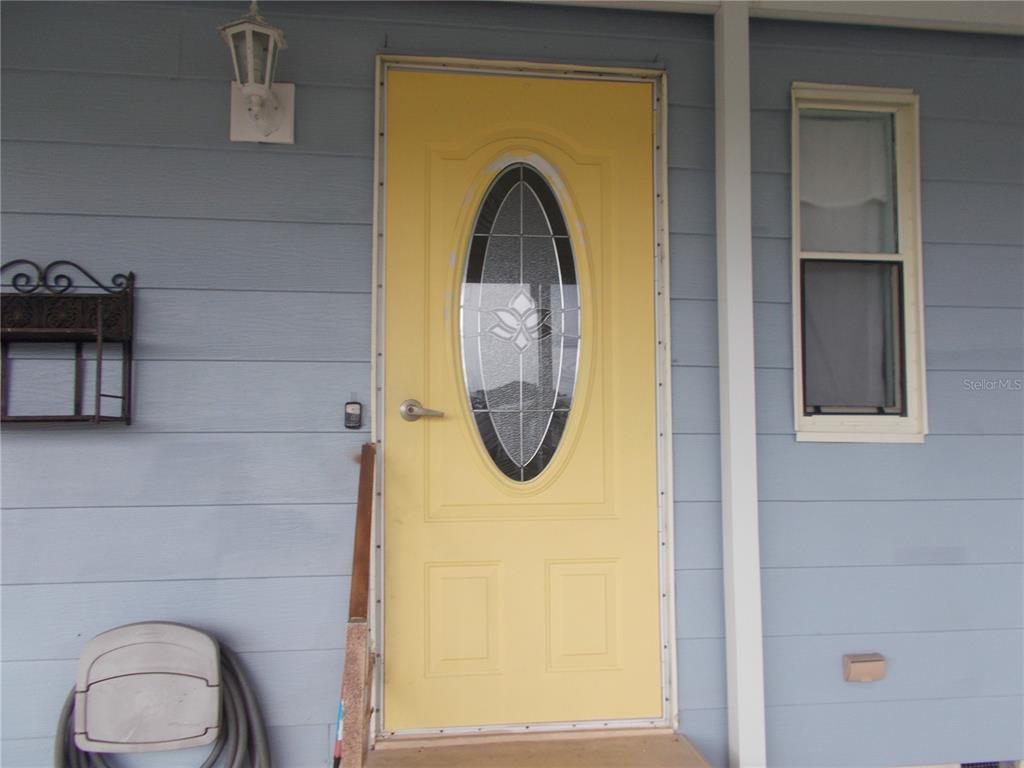A yellow front door with an oval glass insert is set in light blue siding — 6432 KEENA COURT, NORTH PORT, FL