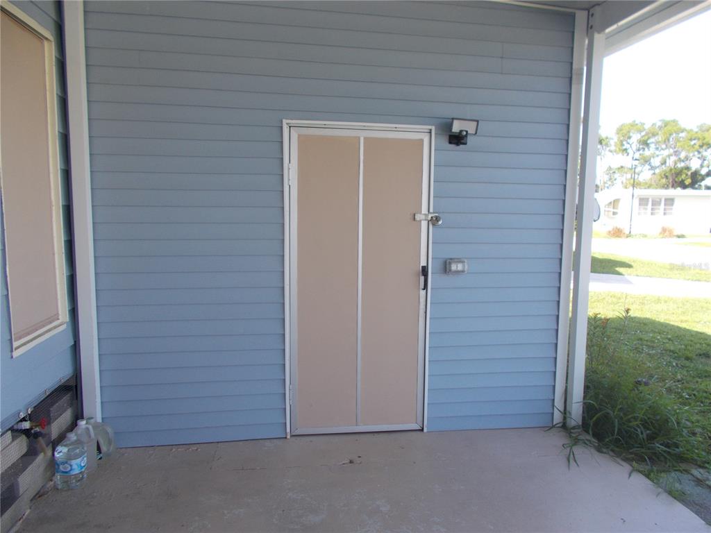 A light blue exterior wall features a beige door with a padlock and a light — 6432 KEENA COURT, NORTH PORT, FL
