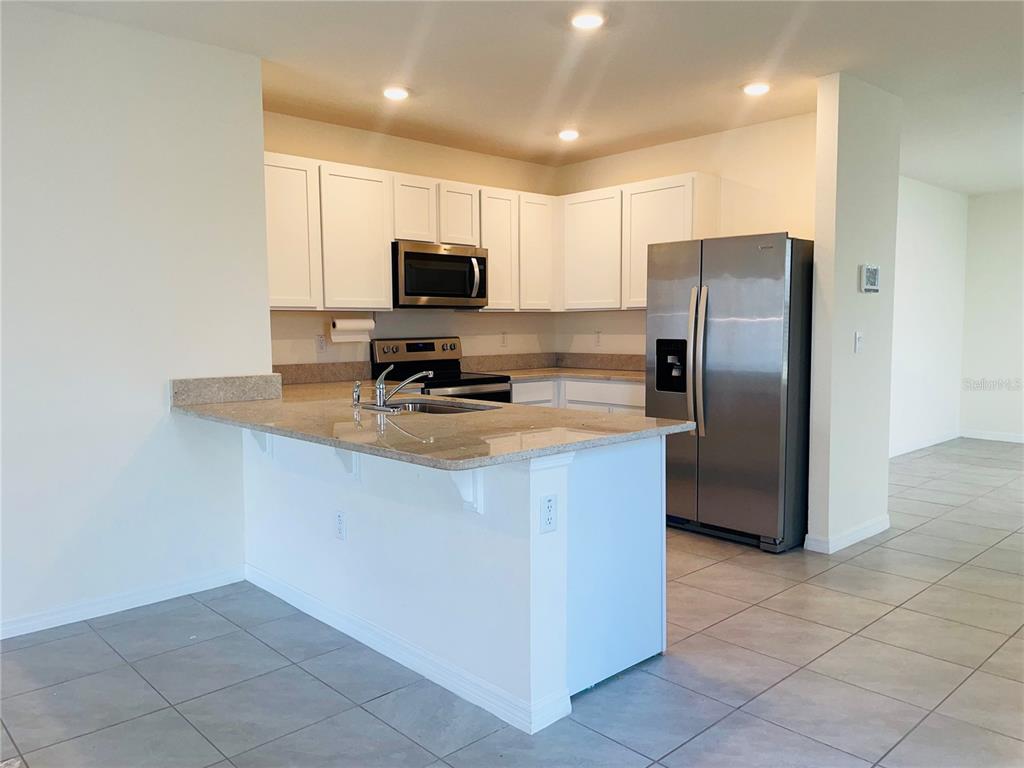A kitchen features white cabinets, stainless steel appliances, and a granite-topped breakfast bar — 17043 OVAL RUM DRIVE, WIMAUMA, FL