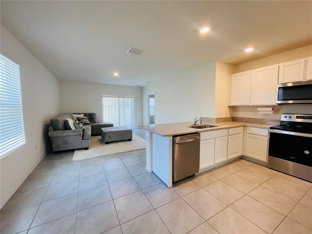 An open-concept kitchen and living area features tile flooring, white cabinets, and stainless steel appliances — 17043 OVAL RUM DRIVE, WIMAUMA, FL