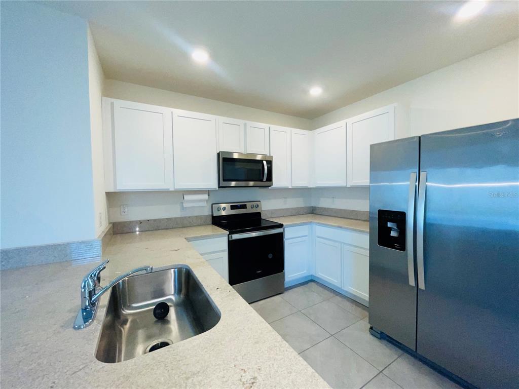 A kitchen features white cabinets, stainless steel appliances, light countertops, and a stainless steel sink — 17043 OVAL RUM DRIVE, WIMAUMA, FL