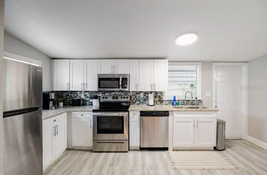 A kitchen features white cabinets, stainless steel appliances, a tiled backsplash, and light wood flooring — 8311 N NEWPORT AVENUE, TAMPA, FL