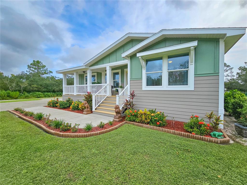 A green and gray manufactured home features a front porch with stairs and landscaping — 875 VOLCO ROAD, EDGEWATER, FL