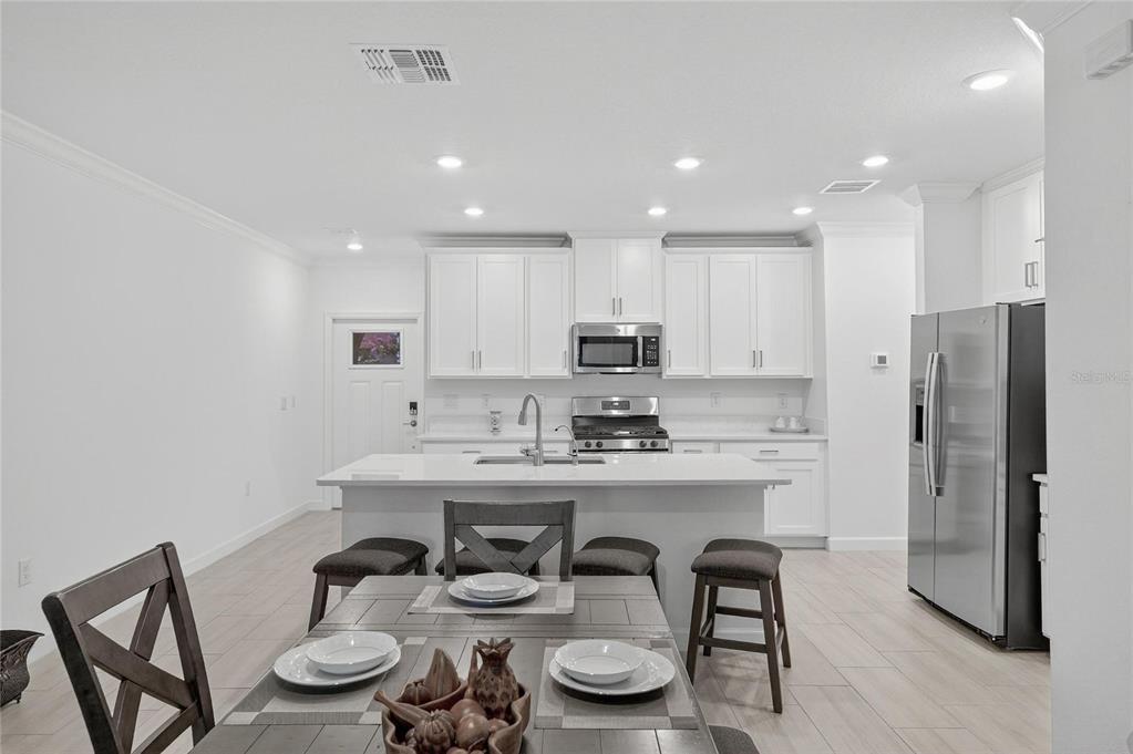 A modern kitchen features white cabinetry, stainless steel appliances, and a central island with seating — 17334 HOLLY WELL AVENUE, WIMAUMA, FL
