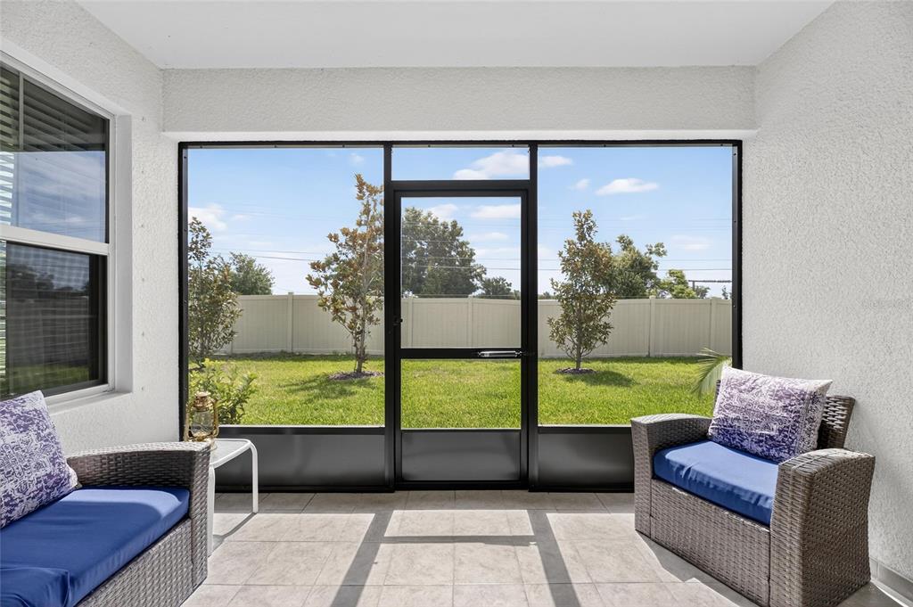 A screened-in patio features tiled flooring, two wicker chairs with blue cushions, and a backyard view — 17334 HOLLY WELL AVENUE, WIMAUMA, FL