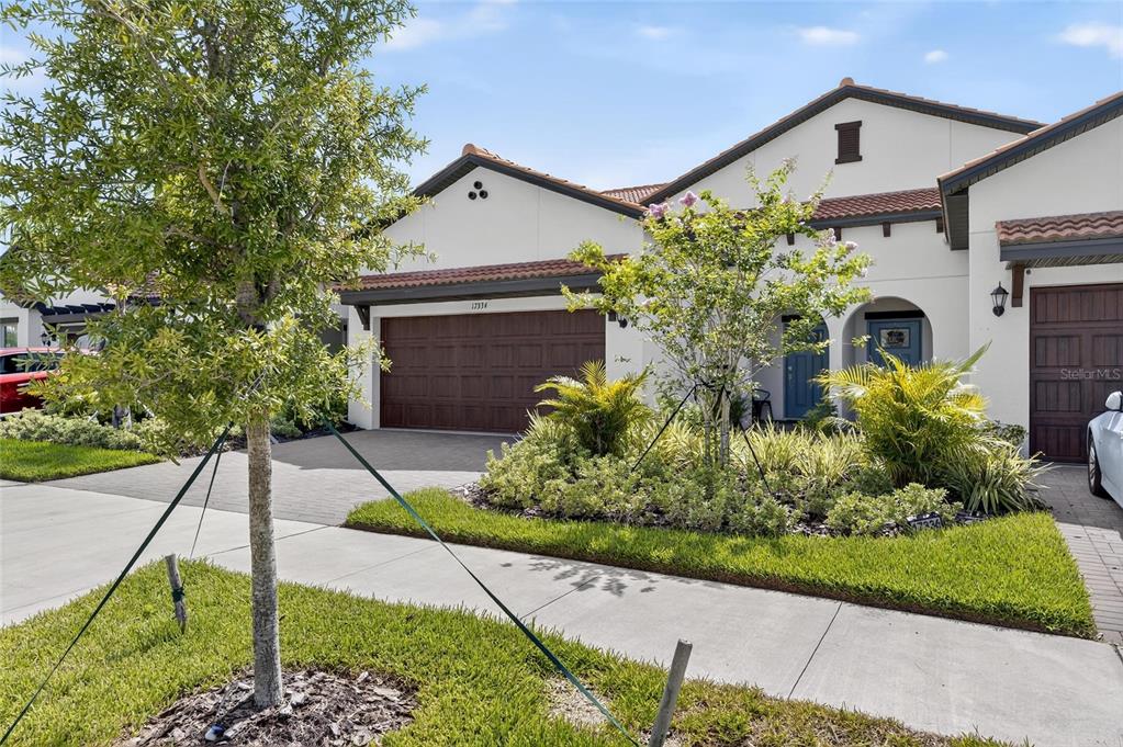 A single-story house with a brown garage door, light stucco walls, and a tiled roof — 17334 HOLLY WELL AVENUE, WIMAUMA, FL