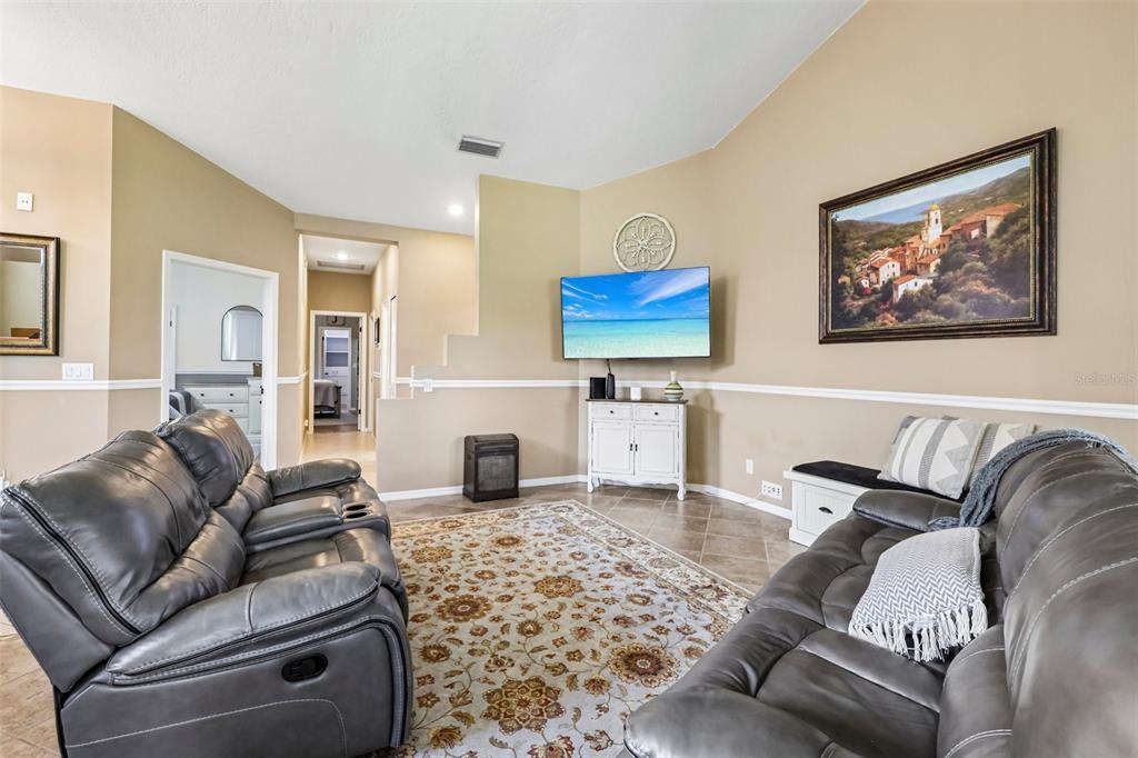 A living room features gray leather reclining sofas, a patterned area rug, and a wall-mounted television — 474 ARROWMOUNT PLACE, LAKE MARY, FL