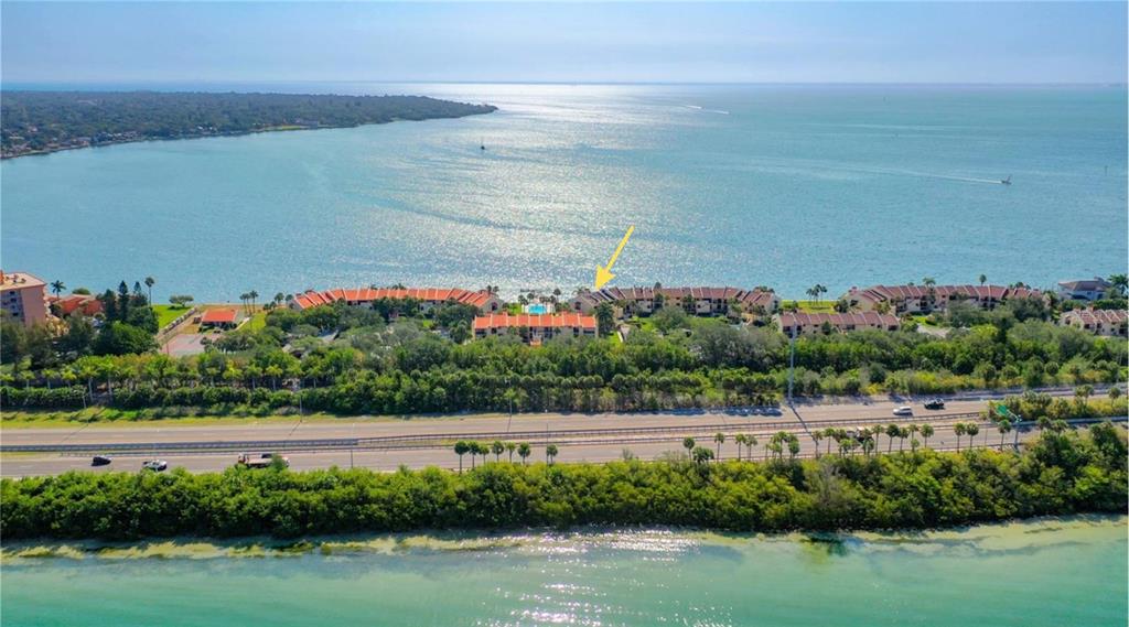 An aerial view shows a waterfront condominium complex with a pool and nearby highway — 7520 SUNSHINE SKYWAY LANE S UNIT T18, ST PETERSBURG, FL