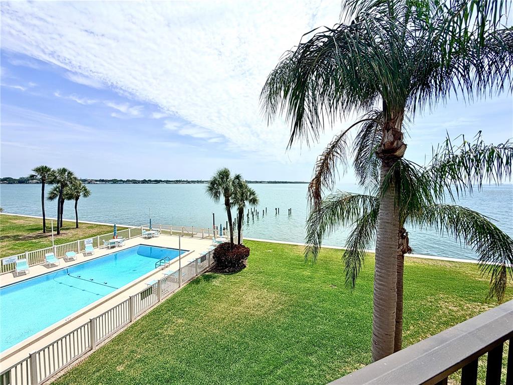 An elevated view of a swimming pool, lawn, palm trees, and a body of water — 7520 SUNSHINE SKYWAY LANE S UNIT T18, ST PETERSBURG, FL
