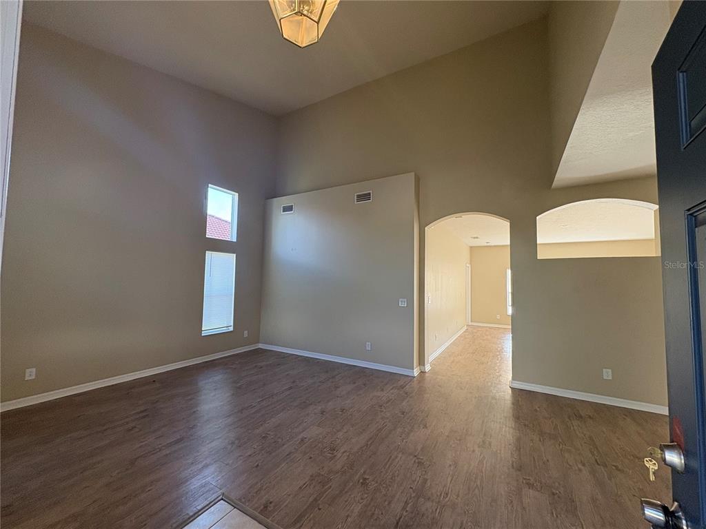 A living room with high ceilings, wood-look flooring, and an arched entryway to a hallway — 6127 46TH STREET E, BRADENTON, FL
