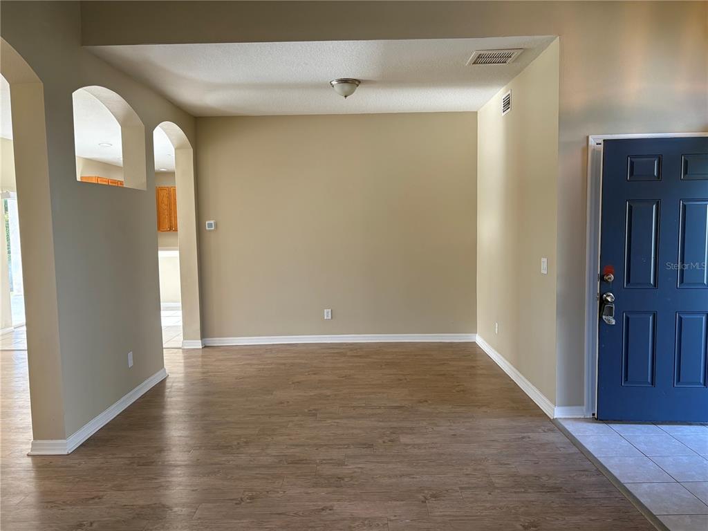 An empty room with wood-look flooring, beige walls, and an arched entryway to the kitchen — 6127 46TH STREET E, BRADENTON, FL