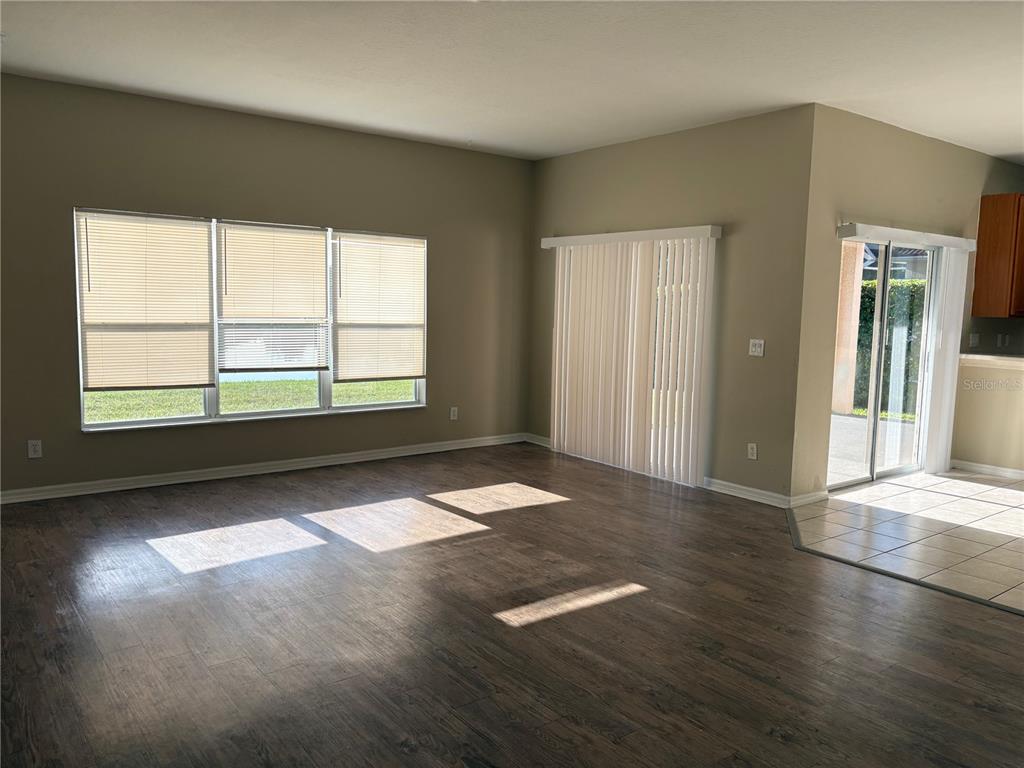 An empty living room features wood-look flooring, large windows with blinds, and a sliding glass door — 6127 46TH STREET E, BRADENTON, FL