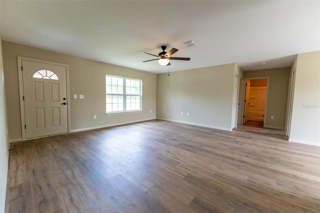 An empty living room features light wood-look flooring, beige walls, a ceiling fan, and a door — 14728 SW 77TH TERRACE, OCALA, FL