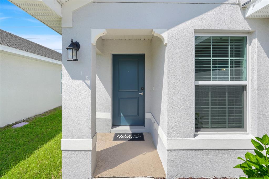 The exterior entrance of a house features a blue front door and a welcome mat — 3768 SAGEFIELD DRIVE, ST CLOUD, FL