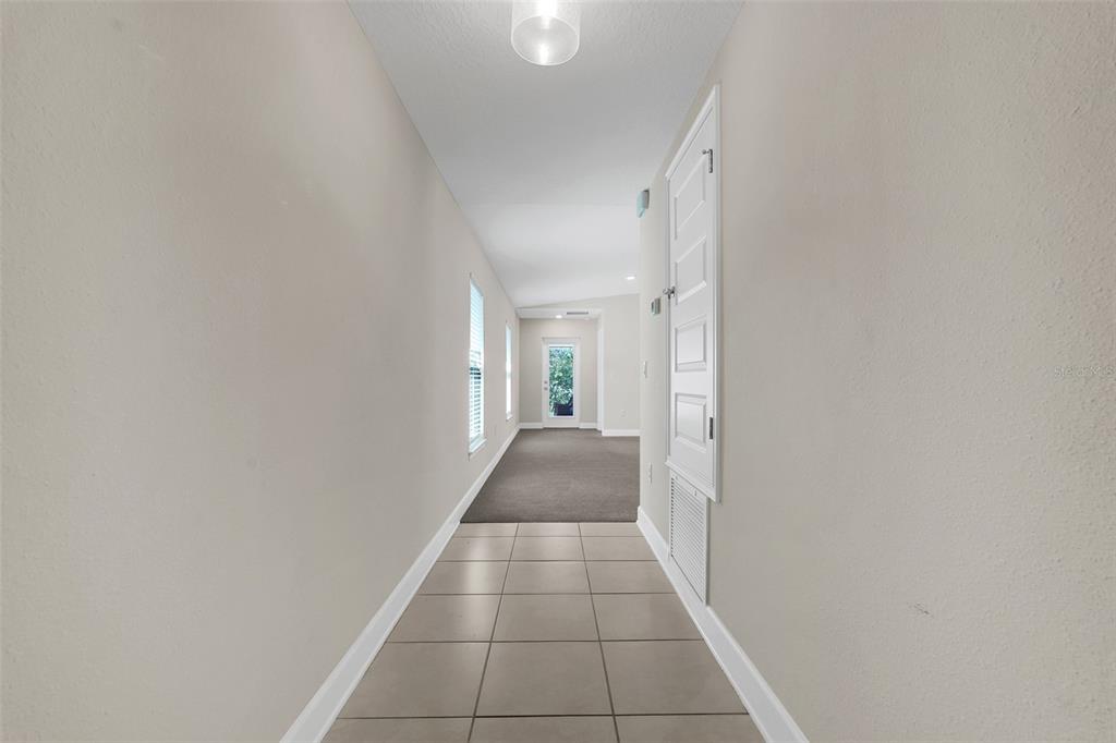 A hallway with tiled flooring leads to a carpeted room with a glass-paneled exterior door — 3768 SAGEFIELD DRIVE, ST CLOUD, FL