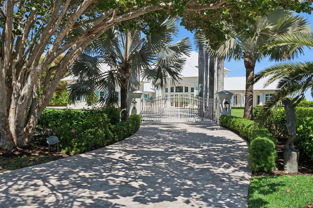 A paved driveway leads through a white metal gate toward a large tropical-style estate home — 716 REEF ROAD, VERO BEACH, FL