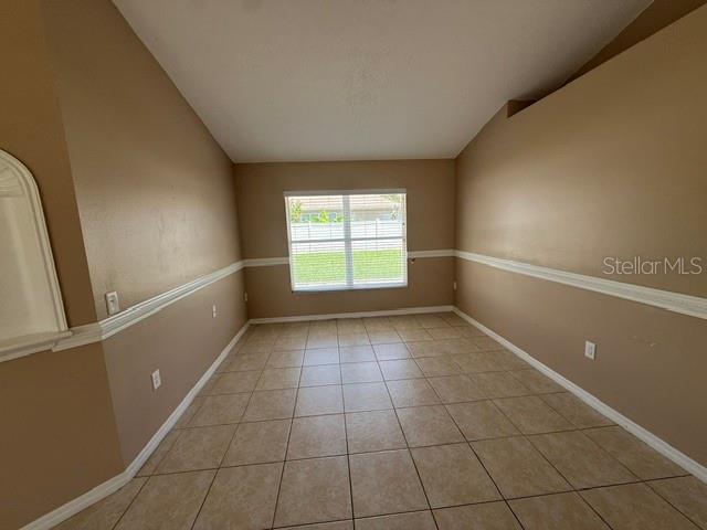 An empty room with tan walls, white chair rail molding, and light-colored tile flooring — 74 ALTERA COURT, KISSIMMEE, FL