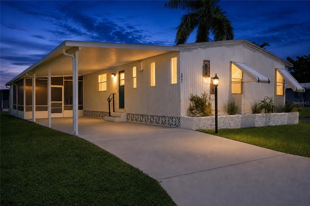 A single-story mobile home with a carport, screened porch, and concrete driveway at dusk — 252 LOON LANE UNIT 252, NAPLES, FL