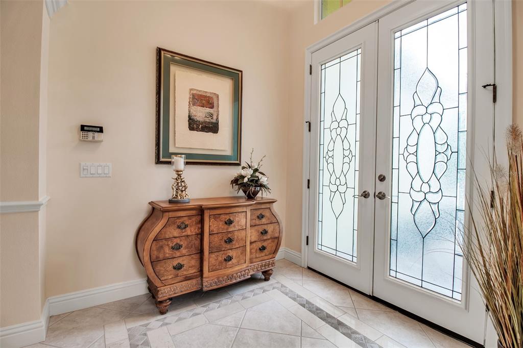 A foyer features a wooden dresser, framed artwork, and double glass-paneled front doors — 21 BAYHEAD LANE, OSPREY, FL