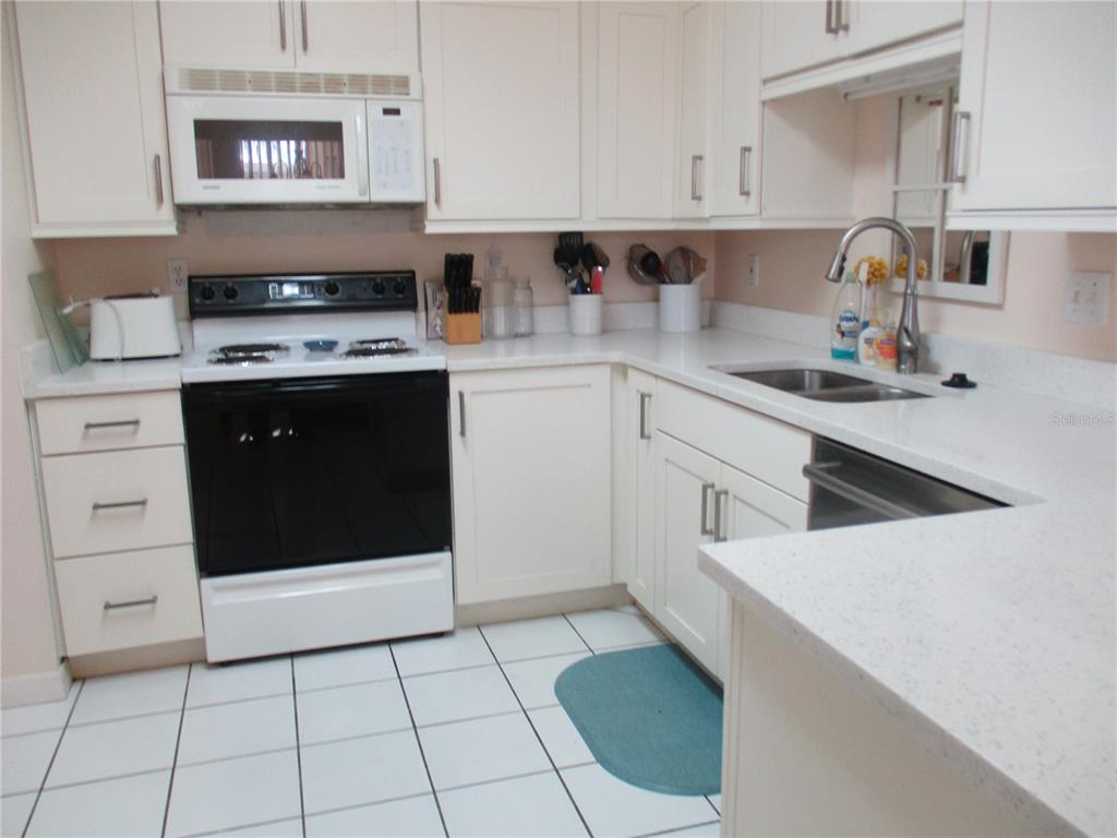 A kitchen with white cabinets, white countertops, a black stove, and white tiled flooring — 1620 FAIRWAY TRACE UNIT A, PALMETTO, FL