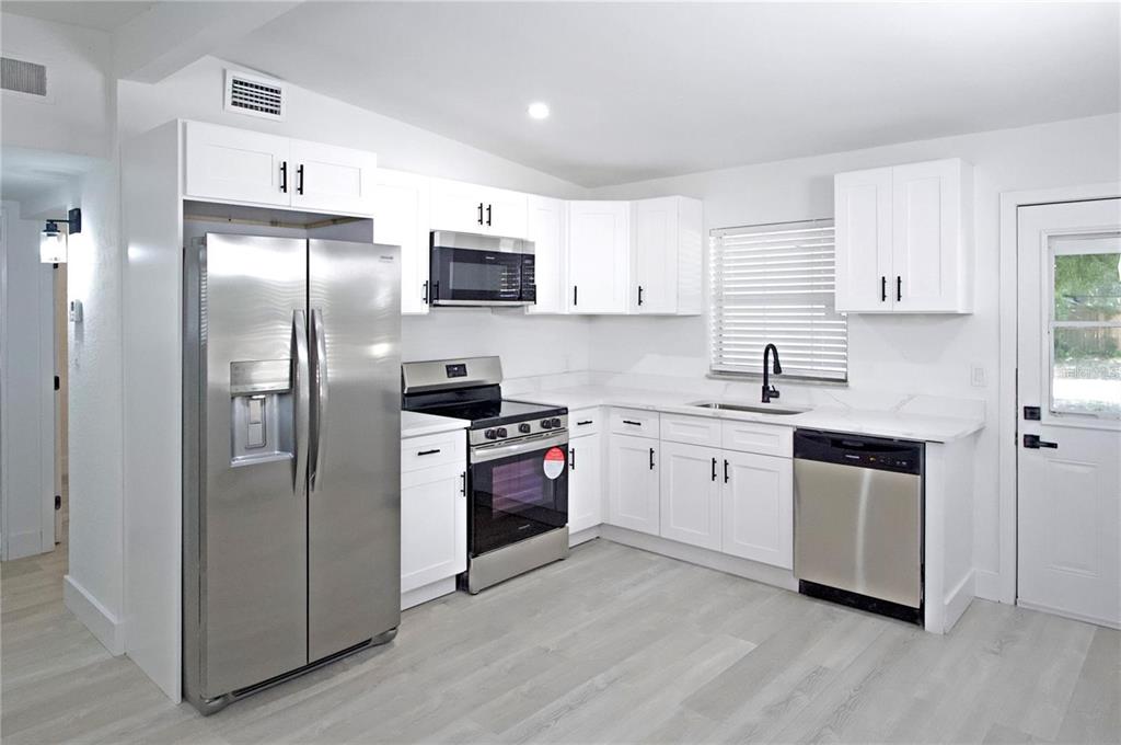 A kitchen features white cabinets, stainless steel appliances, and light-colored wood-look flooring — 9001 82ND STREET, SEMINOLE, FL