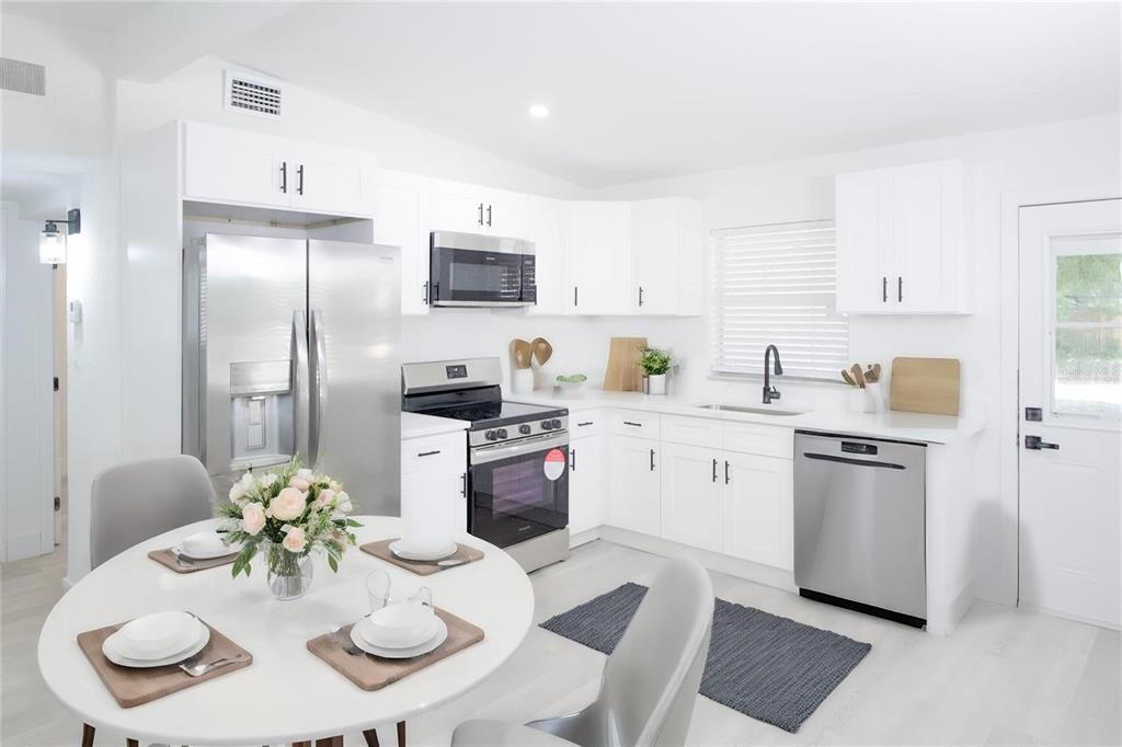 A bright kitchen features white cabinets, stainless steel appliances, and a round dining table — 9001 82ND STREET, SEMINOLE, FL