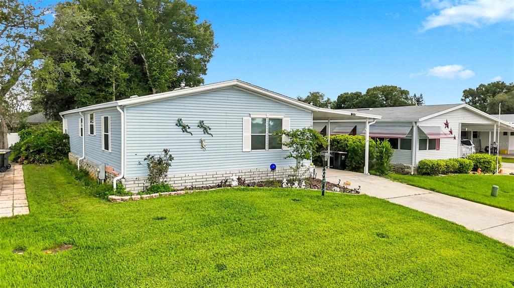 A light blue mobile home with a carport and a green lawn under a blue sky — 6229 KNOTTY PINE DRIVE SE, WINTER HAVEN, FL