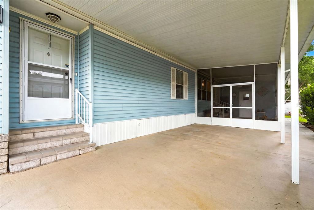 A covered concrete patio features light blue horizontal siding, stone steps, and a screened enclosure — 6229 KNOTTY PINE DRIVE SE, WINTER HAVEN, FL