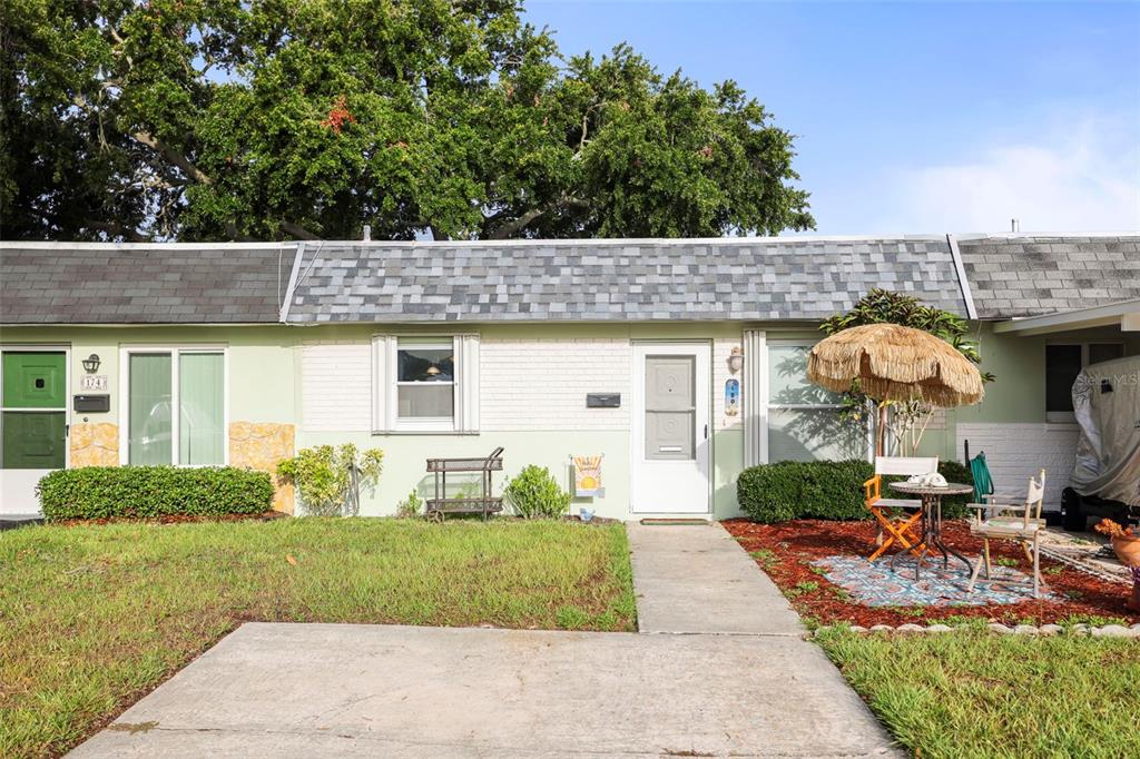 A single-story attached home with a light green exterior, a front walkway, and a patio area — 180 SKY LOCH DRIVE W, DUNEDIN, FL