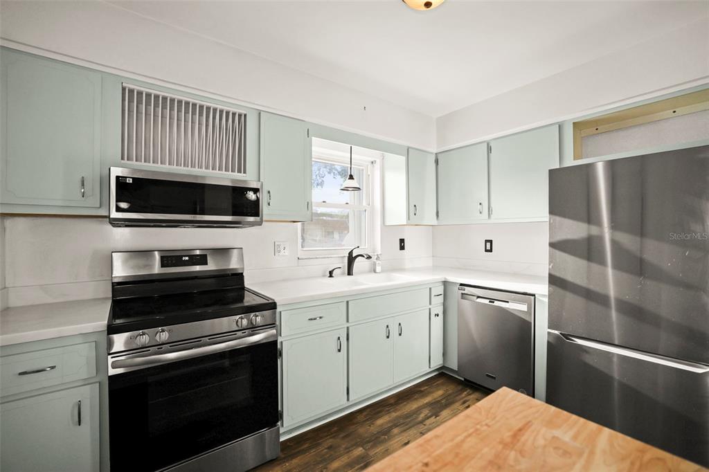 A kitchen features light blue cabinets, stainless steel appliances, white countertops, and wood-look flooring — 180 SKY LOCH DRIVE W, DUNEDIN, FL