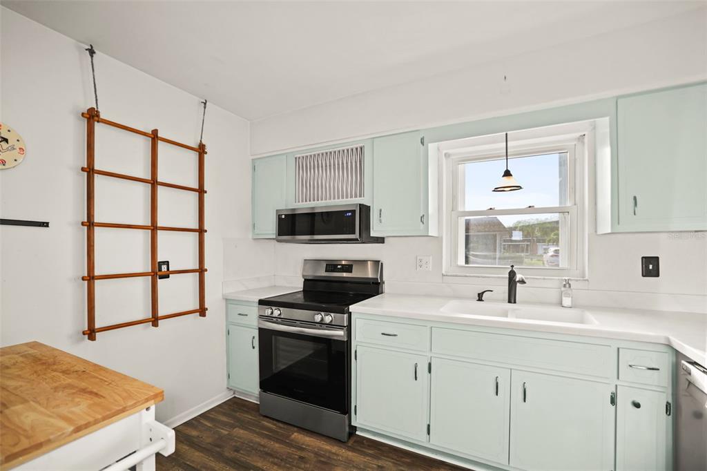 A kitchen features light blue cabinets, stainless steel appliances, a white sink, and wood flooring — 180 SKY LOCH DRIVE W, DUNEDIN, FL