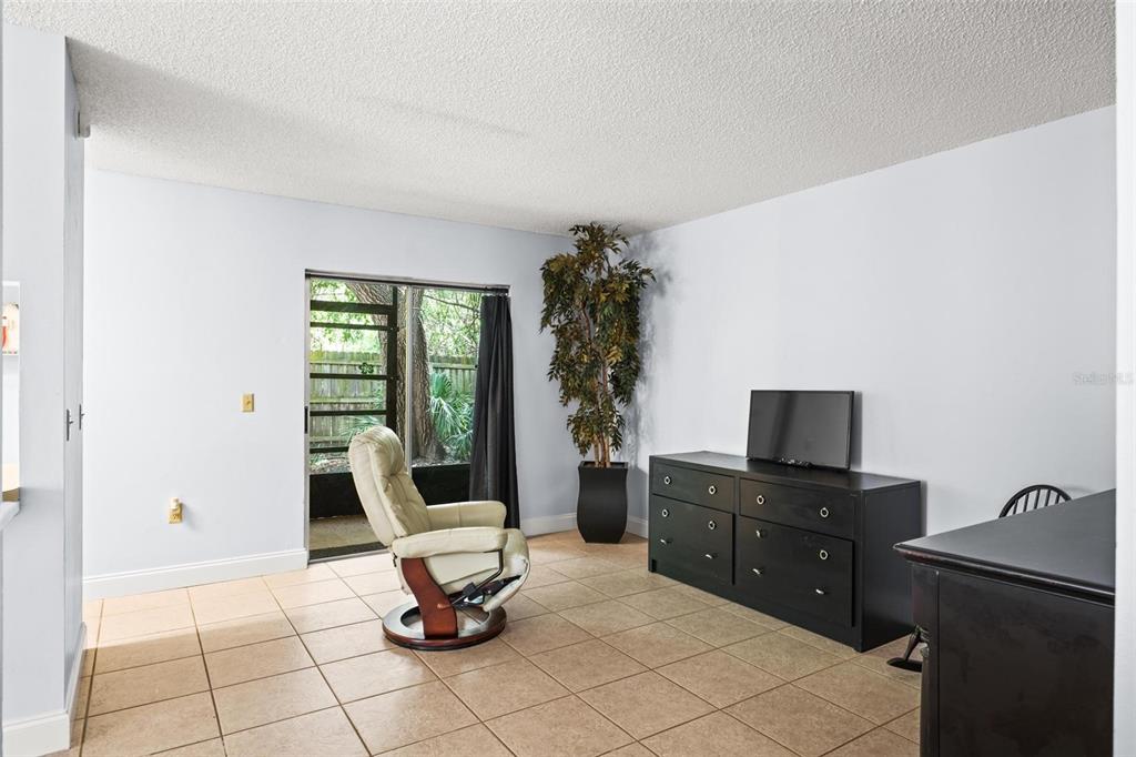 A room with beige tile flooring, a recliner, a black dresser, and a sliding glass door — 265 SPRING DR UNIT 1, MERRITT ISLAND, FL