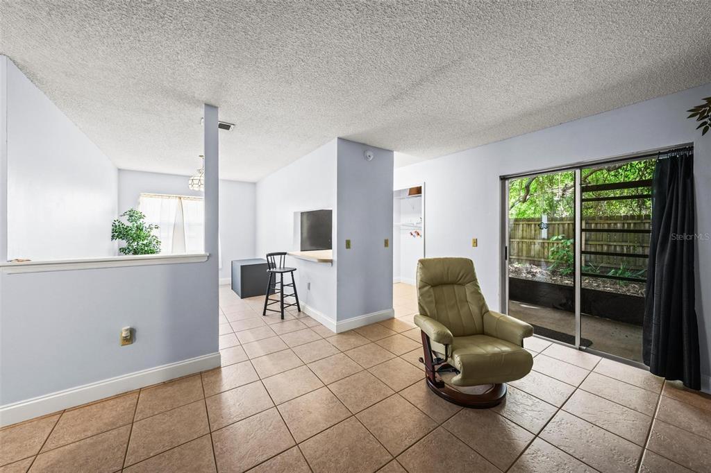A living area with light blue walls, tile flooring, a recliner, and sliding glass patio doors — 265 SPRING DR UNIT 1, MERRITT ISLAND, FL