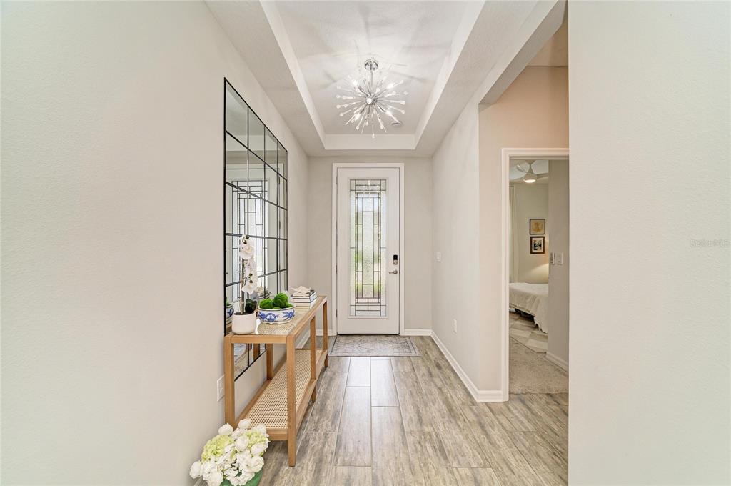 A bright entryway features a wood console table, a large grid mirror, and a chandelier — 4714 ROYCROFT TERRACE, PARRISH, FL