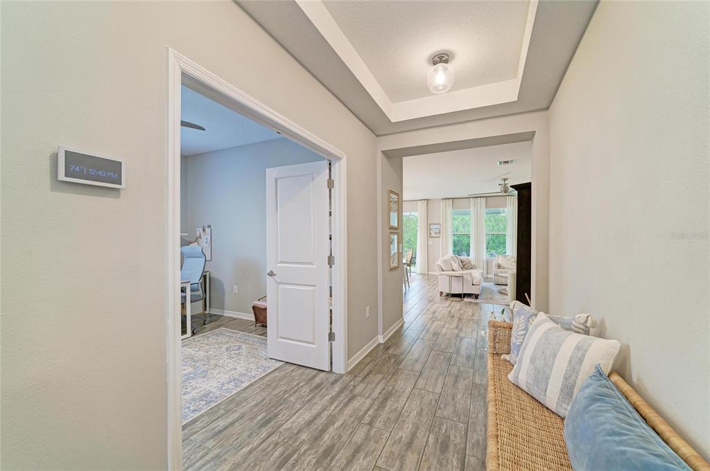 A hallway with wood-look tile flooring leads to a living area and a home office — 4714 ROYCROFT TERRACE, PARRISH, FL